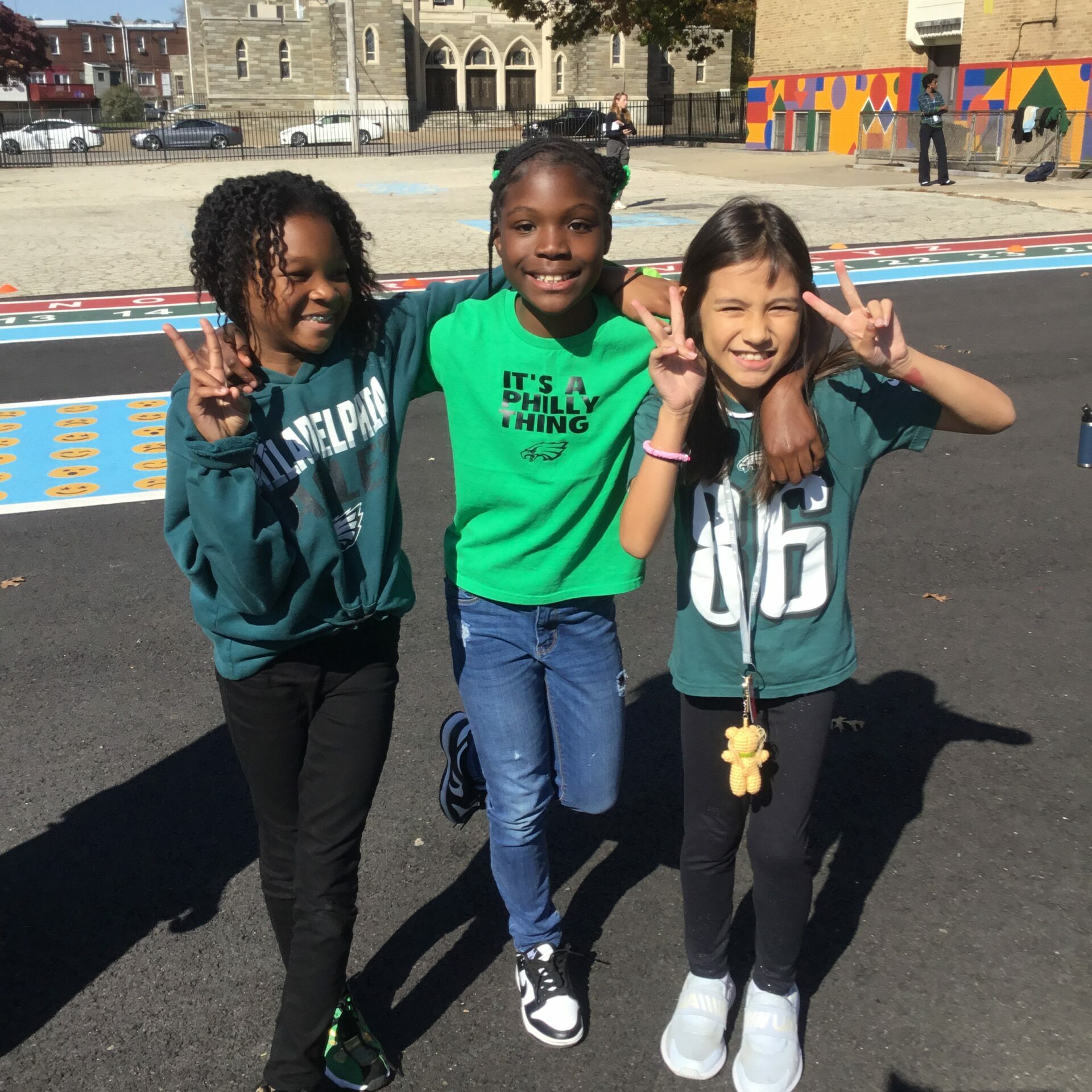 Students Celebrate Eagles Spirit Day Three elementary school students pose together outside on a sunny day, smiling and making peace signs. They are dressed in Philadelphia Eagles gear, celebrating Eagles Spirit Day on their school playground.